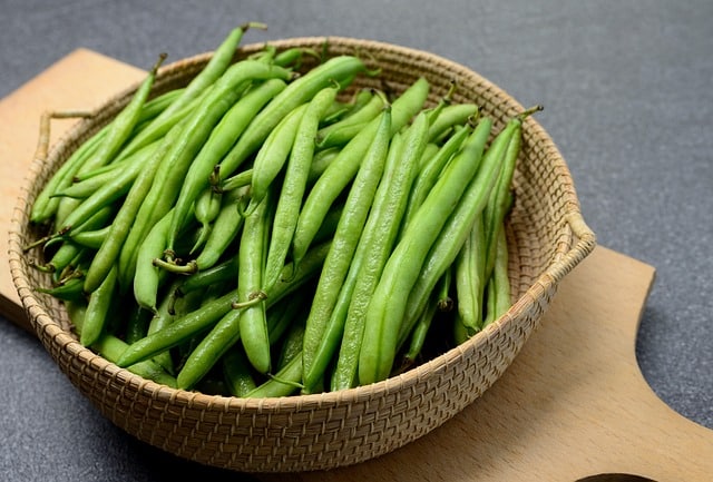 green beans in a basket on top of a wooden cutting board.