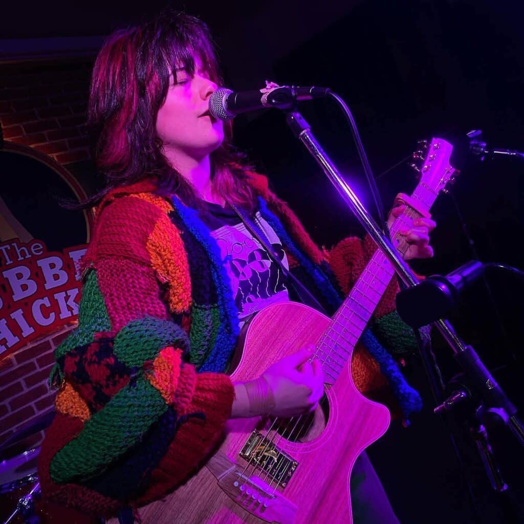 A singer playing guitar and singing under purple pink light in The Rubber Chicken pub