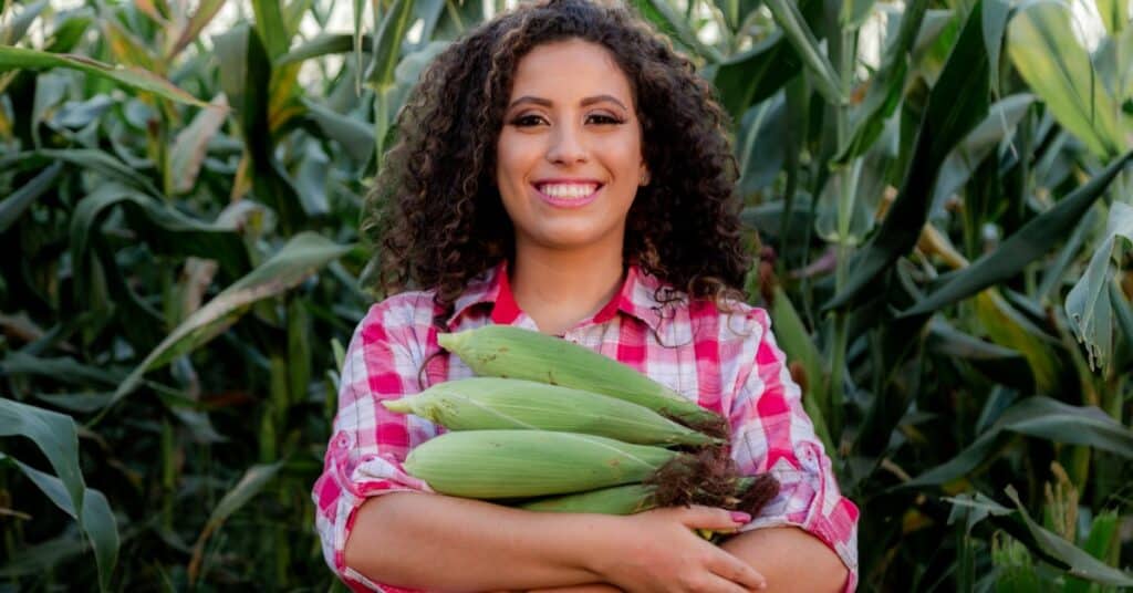 a smily woman holding a bunch of sweet corns.